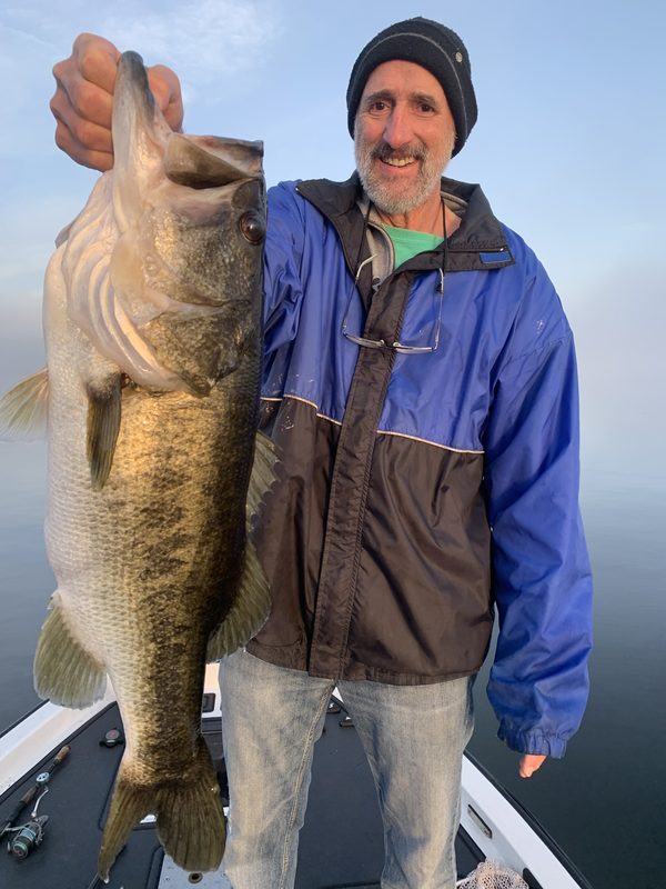 Angler holding a very large largemouth bass on a foggy, windless morning