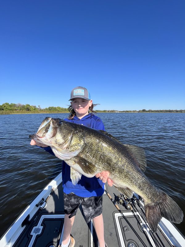 Young angler holding a large largemouth bass with both hands under a deep blue sky