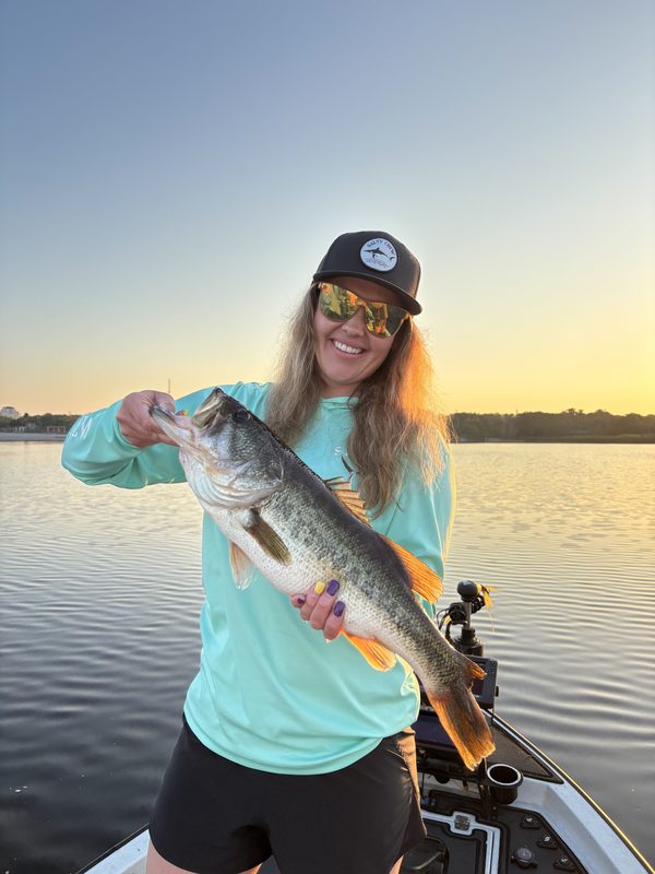 Woman angler holding a largemouth bass at sunrise on a glass-calm Central Florida lake